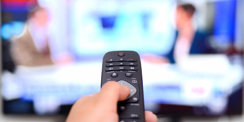 リモコンをテレビに向けている男性の手